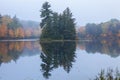 Calm lake and fog in northern Minnesota with trees in autumn color and pines on a small island Royalty Free Stock Photo