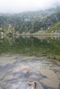 Calm lake in mountains with clear water, with reflection of rocky mountains on surface on foggy day Royalty Free Stock Photo