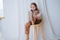 Calm little girl sitting on a stool at home, she`s puting on sandals Royalty Free Stock Photo