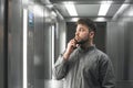 Calm male office worker is talking by smartphone in the elevator. Peaceful businessman is communicating with clients via phone and