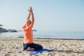 Calm man sitting in Seiza position, doing deep breathing exercises and meditating in early morning hours on the sandy beach with