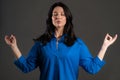 Calm mature woman relaxing, meditating. Adult lady calms down, breathes deeply with mudra om on grey studio background Royalty Free Stock Photo