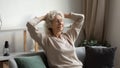 Calm mature woman stretching, relaxing on cozy couch at home