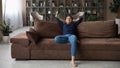 Calm millennial indian woman sit on sofa hands behind head