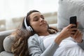 Calm mixed race millennial woman lying on sofa with headphones.