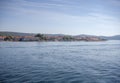 Calm ocean with glistening water and a coastal town in the horizon under a cloudy sky