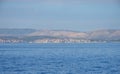 Calm ocean with glistening water and a coastal town and mountains in the horizon