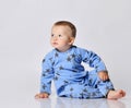 Calm barefooted blond baby boy toddler in blue fleece jumpsuit with stars sits on the floor leaning on his arm
