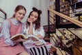 Calm and peaceful girls sitting shoulder to shoulder and reading book