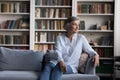 Calm pensive aged woman sit on sofa in living room