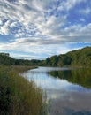 Calm pond or lake with low hills, marsh grasses and dramatic blue sky with clouds Royalty Free Stock Photo