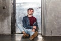 Calm relaxed model man in bright red sunglasses and denim casual style, sitting near metallic door, Royalty Free Stock Photo