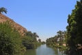 Calm river surrounded by trees and palms with a rocky mountain on the side in a small village