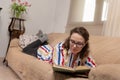 Calm satisfied Caucasian woman relaxing on comfortable couch alone, holding paper book, spending weekend