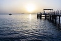 calm sea at dawn with pink clouds on the horizon and wooden pier and ship in the distance Royalty Free Stock Photo