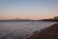 Calm sea and the sandy beach with a wooden dock and mountains against the pink sunset