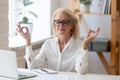 Calm senior businesswoman practice yoga in office