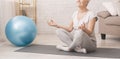 Calm senior lady practicing yoga, meditating at home