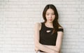Calm serious beautiful Asian woman wearing off shoulder black and posing with crossed arms and looking at camera on white brick Royalty Free Stock Photo