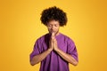 Calm serious black adult curly man with closed eyes in purple t-shirt prays with hands