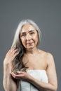 Calm serious old european female with gray hair touches fingers to hair, enjoy result of treatment