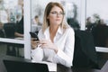 Calm serious young attractive blonde uses phone while working at table in office