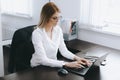 Calm serious young attractive blonde woman uses laptop to work at table in office