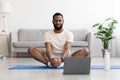 Calm smiling young black bearded guy practicing yoga, doing leg exercises on floor on mat in living room
