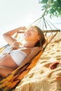 Calm smiling young woman lying in hammock in bright sun light