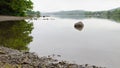 A calm and still Coniston water with a boulder in close focus