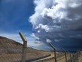 The calm and the storm in the same photo, with clear skies and approaching storm clouds, seen from a fence