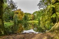 Early autumn view of a pond surrounded by autumnal coloured trees.buret through the trees.. Royalty Free Stock Photo