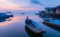 Calm waters reflect a sublime sunset at a peaceful fishing village, with traditional boats moored beside rustic stilt Royalty Free Stock Photo