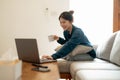 Calm young asian female working at laptop sitting on sofa, happy girl browsing internet or shopping online during sunny Royalty Free Stock Photo