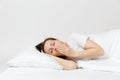 Calm young brunette woman lying in bed with white sheet, pillow, blanket on white background. Yawning beauty female Royalty Free Stock Photo