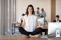 Calm young businesswoman doing yoga exercise at work desk