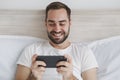 Calm young handsome bearded man lying in bed with white sheet pillow blanket in bedroom at home. Male spending time in