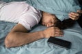 Calm young man in pajamas lying in bed sleep near cell phone, relax at home in bedroom. Good mood night morning bedtime Royalty Free Stock Photo