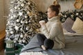 Calm young woman enjoying drinking tea or coffee in living room with Christmas decor over new year tree background Royalty Free Stock Photo