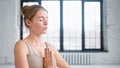 Calm young woman with hair bun in beige top does yoga breathing exercises holding hands in namaste mudra in studio Royalty Free Stock Photo