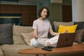 Calm young woman meditate, relax, sitting on sofa in lotus pose during online yoga lesson with laptop at home Royalty Free Stock Photo