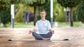 Calm young woman sitting in lotus pose on mat during morning meditation in park