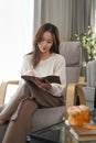 Calm young woman wearing warm sweater relaxing on armchair and reading book. Winter, coziness, leisure and people