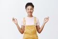 Calming down and getting rid of stress inside. Calm and cute good-looking dark-skinned female in yellow trendy overalls