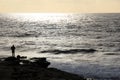 Beautiful sunset with expanse of ocean and man standing on the rocks