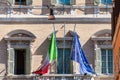 Calmly hanging Italian and European Union flags against the background of a richly decorated building