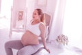 Young beaming long-haired pregnant woman in a white t-shirt looking calm Royalty Free Stock Photo