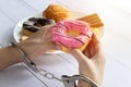 Calories control, food diet and weight loss concept. top view of two hands was control by handcuff, holding doughnut Royalty Free Stock Photo