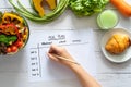 Calories control, meal plan, food diet and weight loss concept. top view of hand filling meal plan on weekly table with salad Royalty Free Stock Photo