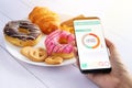 Calories counting and food control concept. woman using Calorie counter application on her smartphone with doughnut ,snack